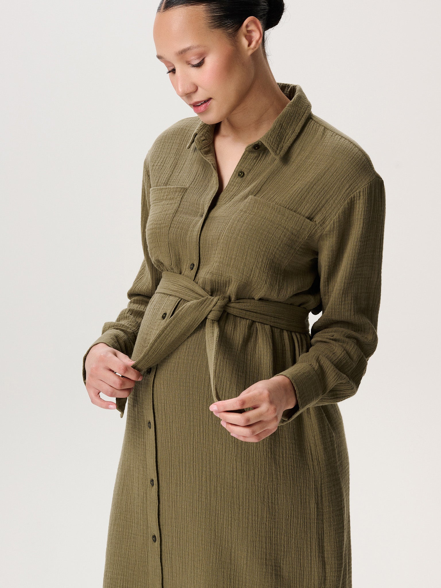 Noppies Umstandskleid kaufen oder mieten Mutterkleid. Schwangere Frau mit Musselin Umstandskleid in oliv. Detailaufnahme vom Stoff und Bindegürtel über dem Babybauch