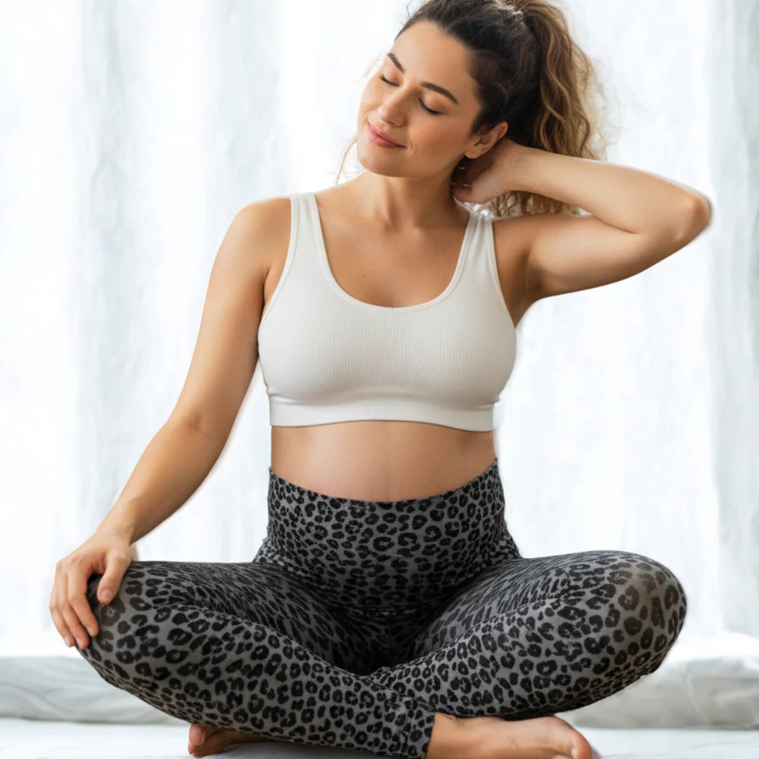 Model sitzt im Schneidersitz - Umstandsleggings Leoprint grau-schwarz mit hohem Bauchbund über Babybauch