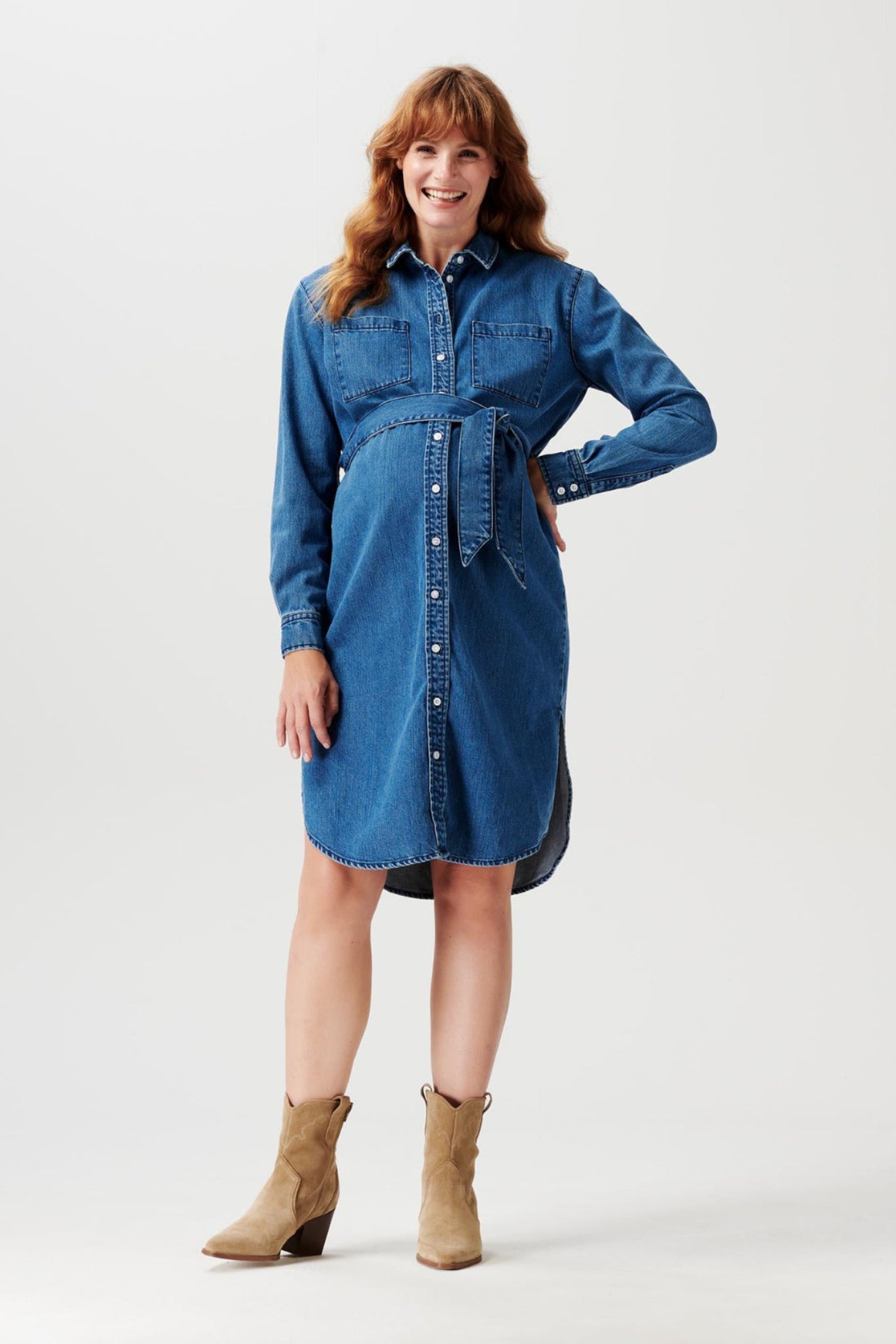 Lächelnde Schwangere trägt Noppies Denim Umstandskleid und Cowboy Boots, Umstandskleid bei Mutterkleid kaufen oder mieten