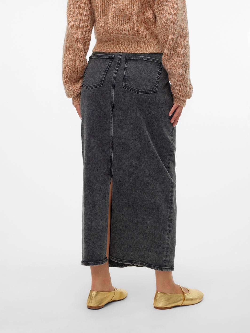 Model zeigt Mamalicious Umstandsjeansrock mit aufgesetzten Hosentaschen und in dunkelgrau. Sie trägt goldene flache Schuhe. Umstandsrock bei Mutterkleid zu kaufen.