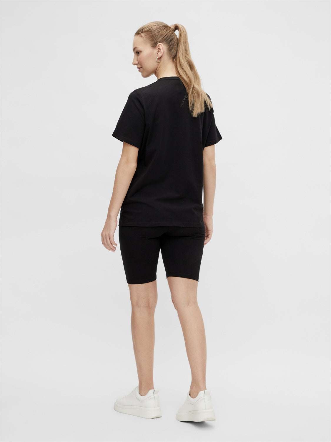 Blondes Model zeigt von hinten das Umstandsmode TShirt und Umstands Radlerhose von Mamalicious. Bei Mutterkleid kaufen oder mieten