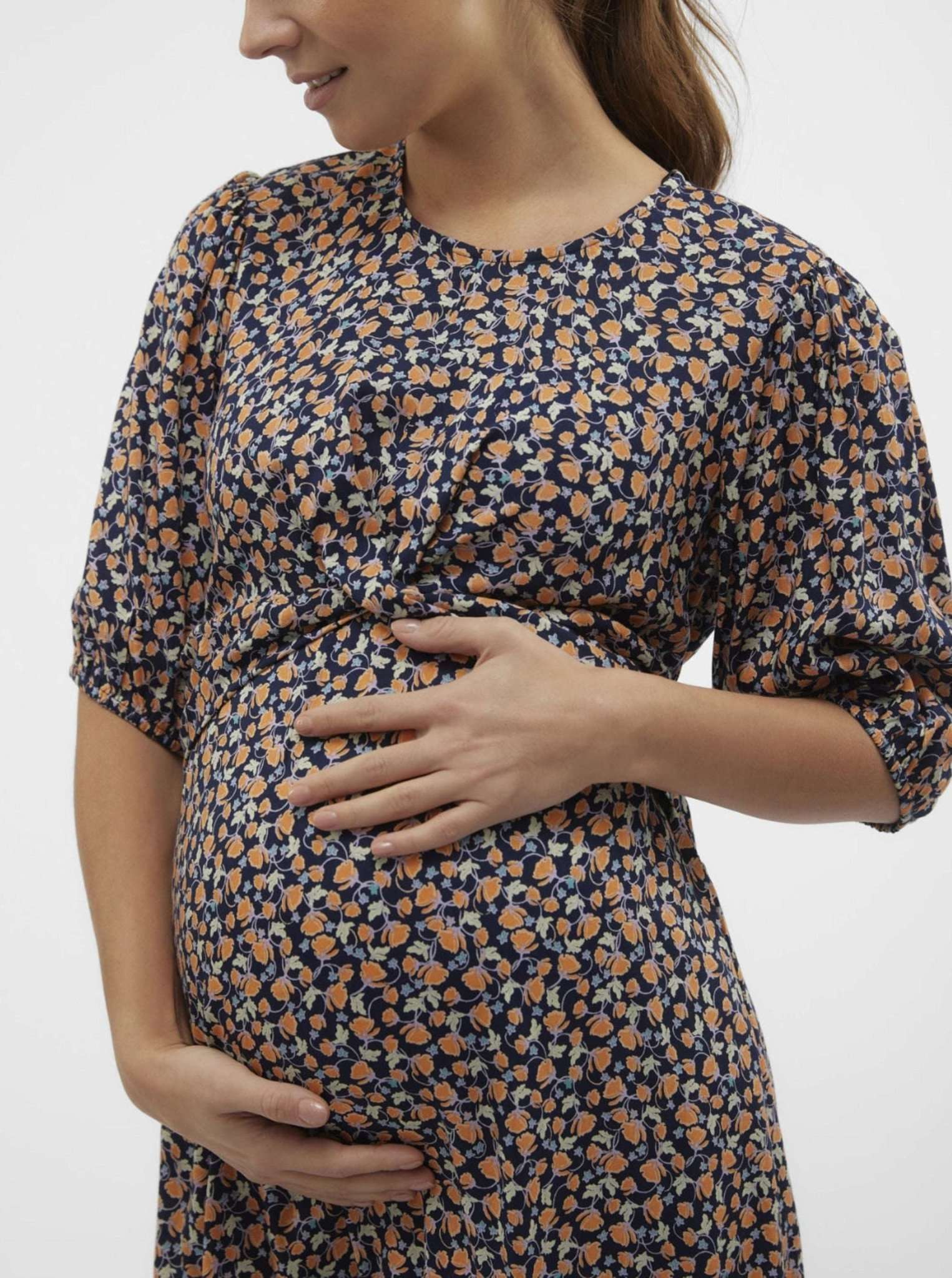 Brünettes Model zeigt in Nahaufnahme Mamalicious Schwangerschaftskleid mieten oder kaufen bei Mutterkleid. Kurzarm mit Knotendetail.