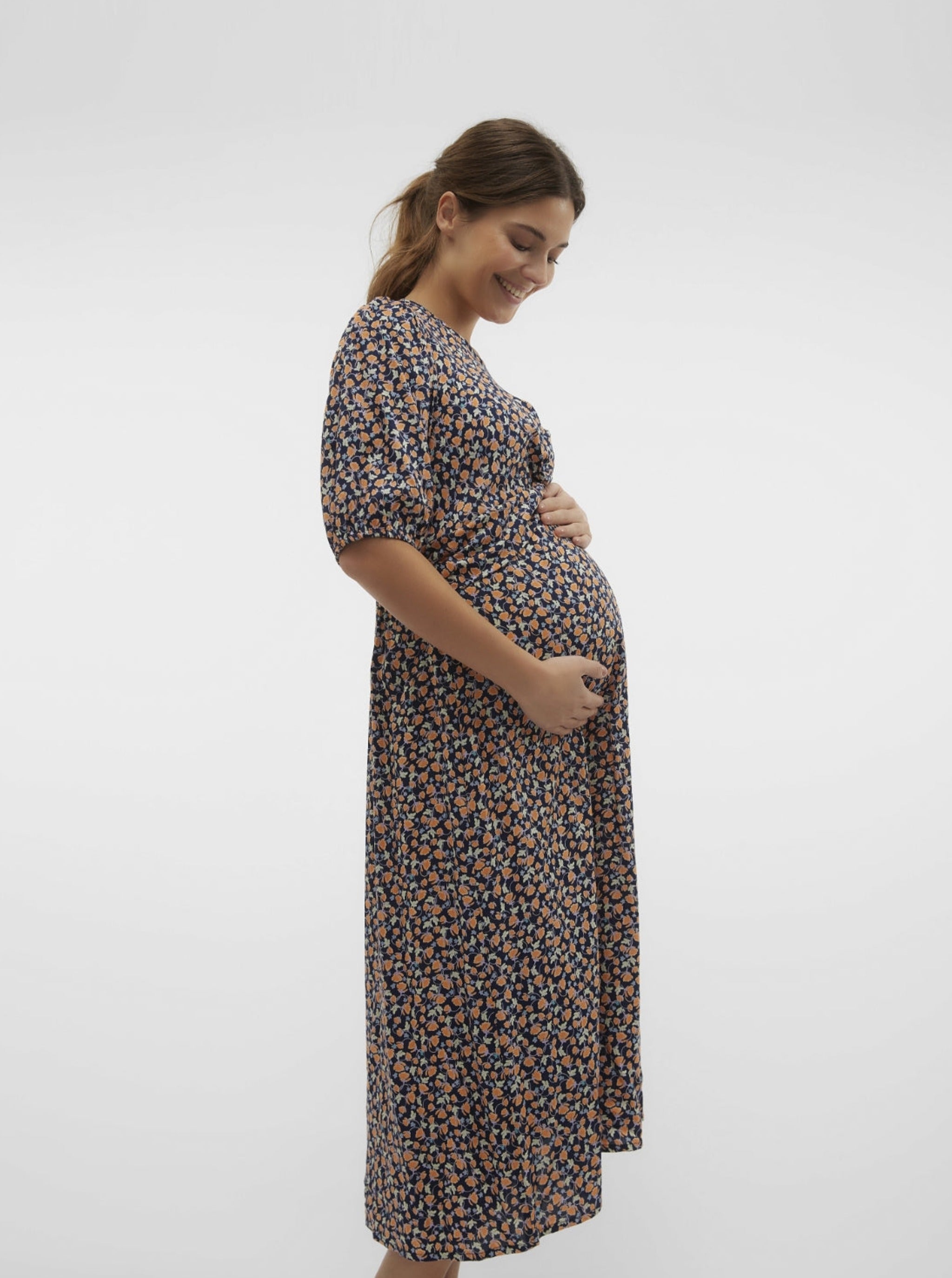Model lächelt und zeigt Mamalicious Umstandskleid im Blumenprint kaufen oder mieten bei Mutterkleid. Für die Schwangerschaft, mit Kurzarm.