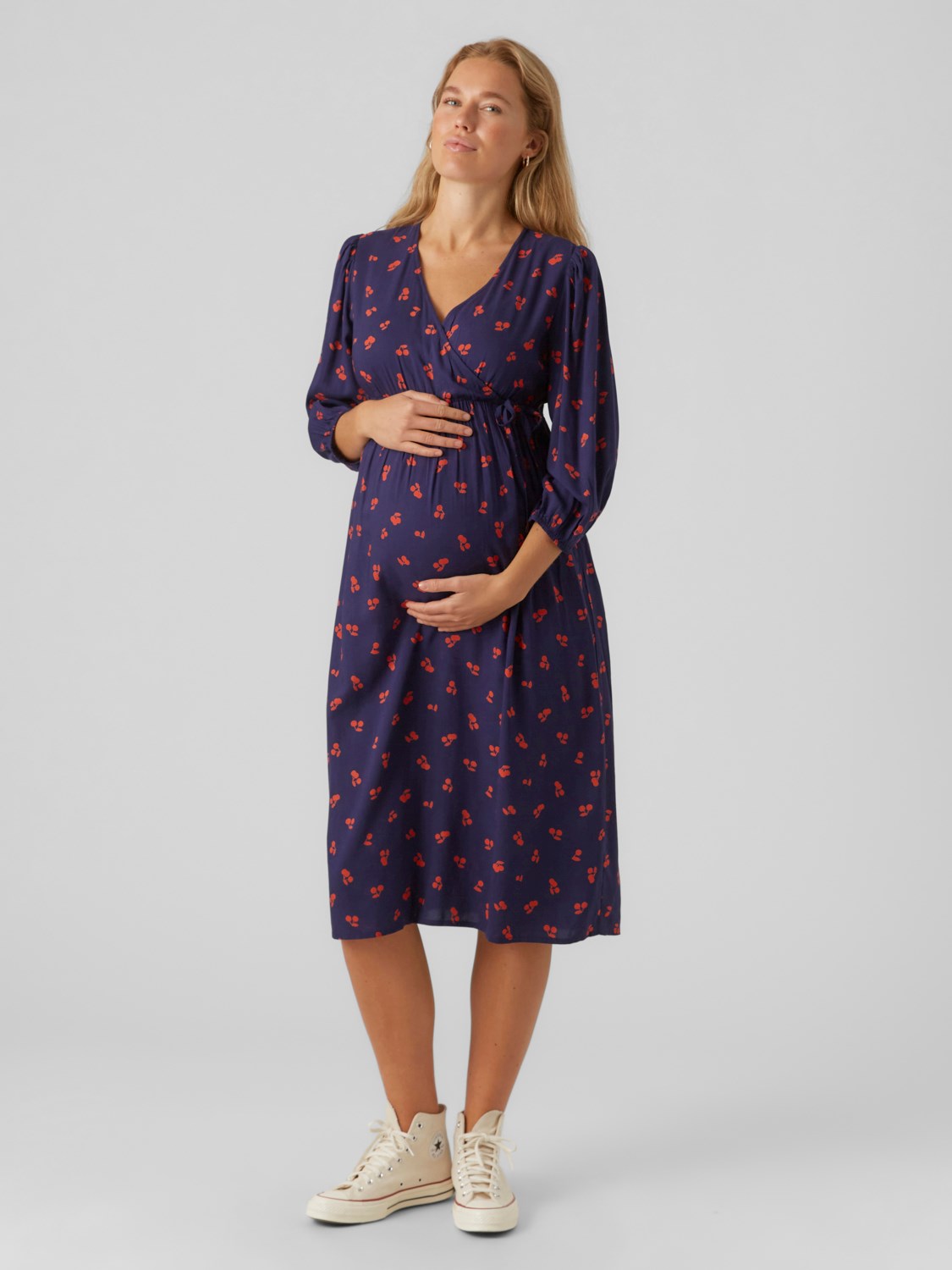 Mamalicious Umstandskleid mieten und online kaufen bei Mutterkleid Allover Kirschprint navy Midilänge Wickelausschnitt V-Form. Blondes Model zeigt Umstandsmode von vorne in Ganzkörper.