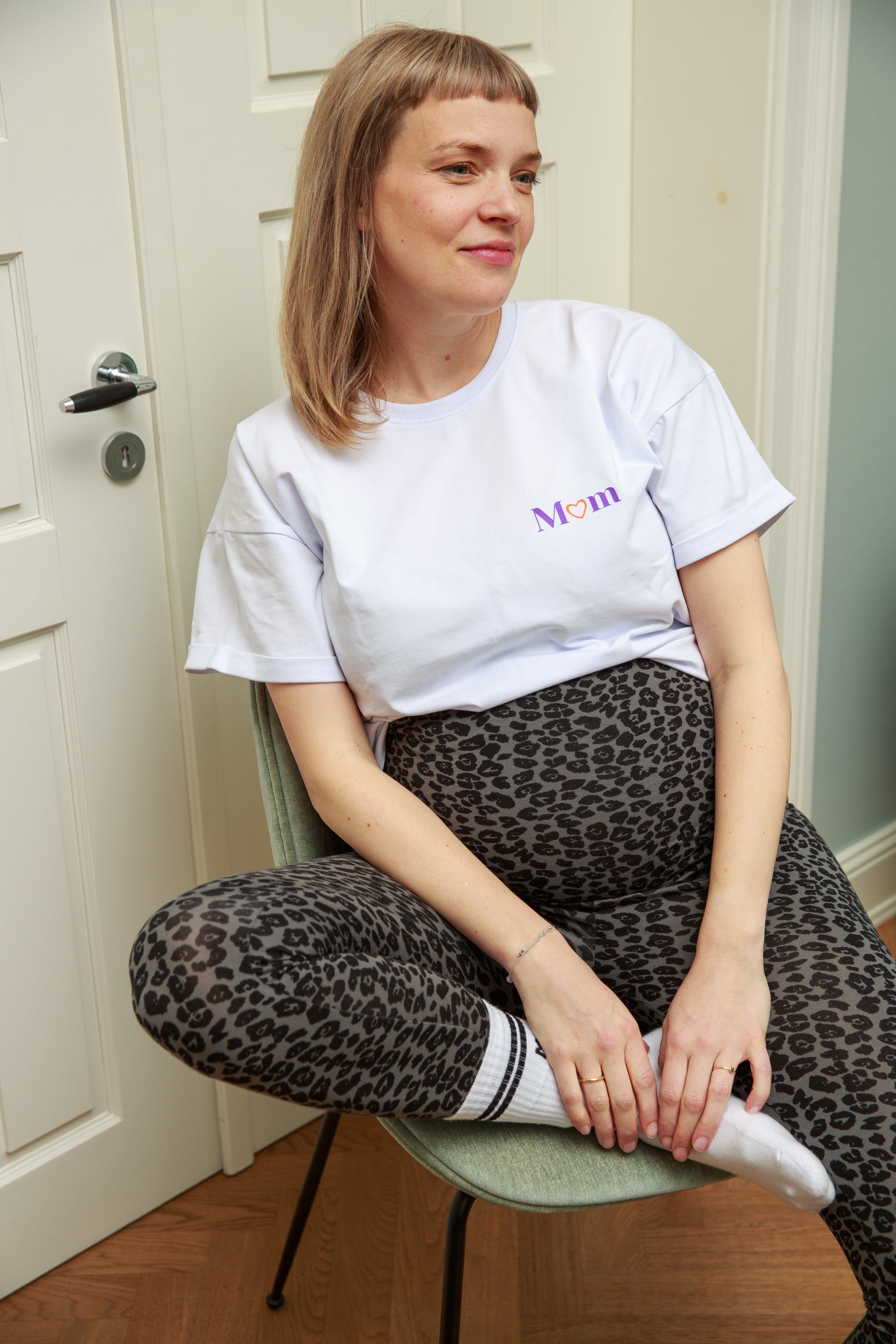 Model schwanger sitzt auf Stuhl mit Leo Leggings in grau schwarz und weißem Still-T-Shirt kombiniert mit Mom Socken