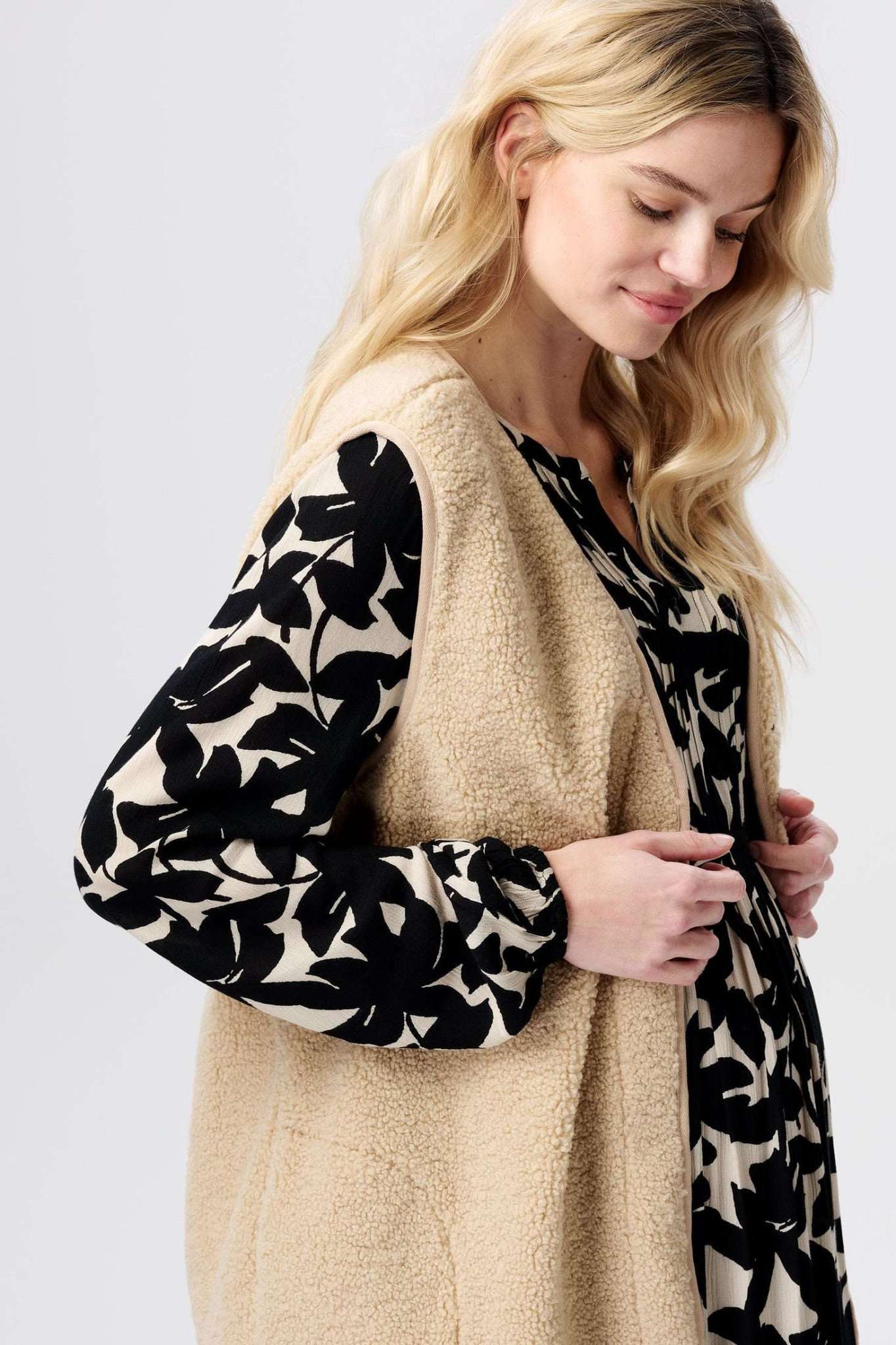 Schwangere Frau im Profil zeigt eine flauschige Noppies Teddy Umstandsweste in Creme. Bei Mutterkleid kaufen oder mieten.