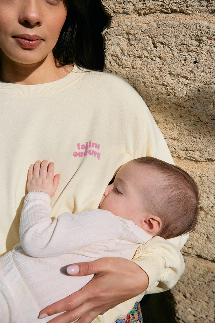 Stillende Mama im Sweatshirt von Tajinebanane, gelb mit Rosa Schriftzug. Online mieten oder kaufen bei Mutterkleid