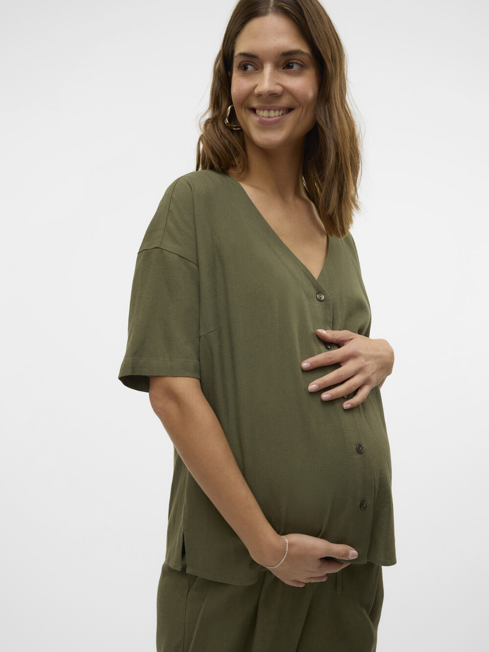Brünettes Model lächelt in die Ferne in einer grünen Vero Moda Maternity Umstandsbluse Stillbluse mit Händen am Babybauch. Bei Mutterkleid mieten oder kaufen.