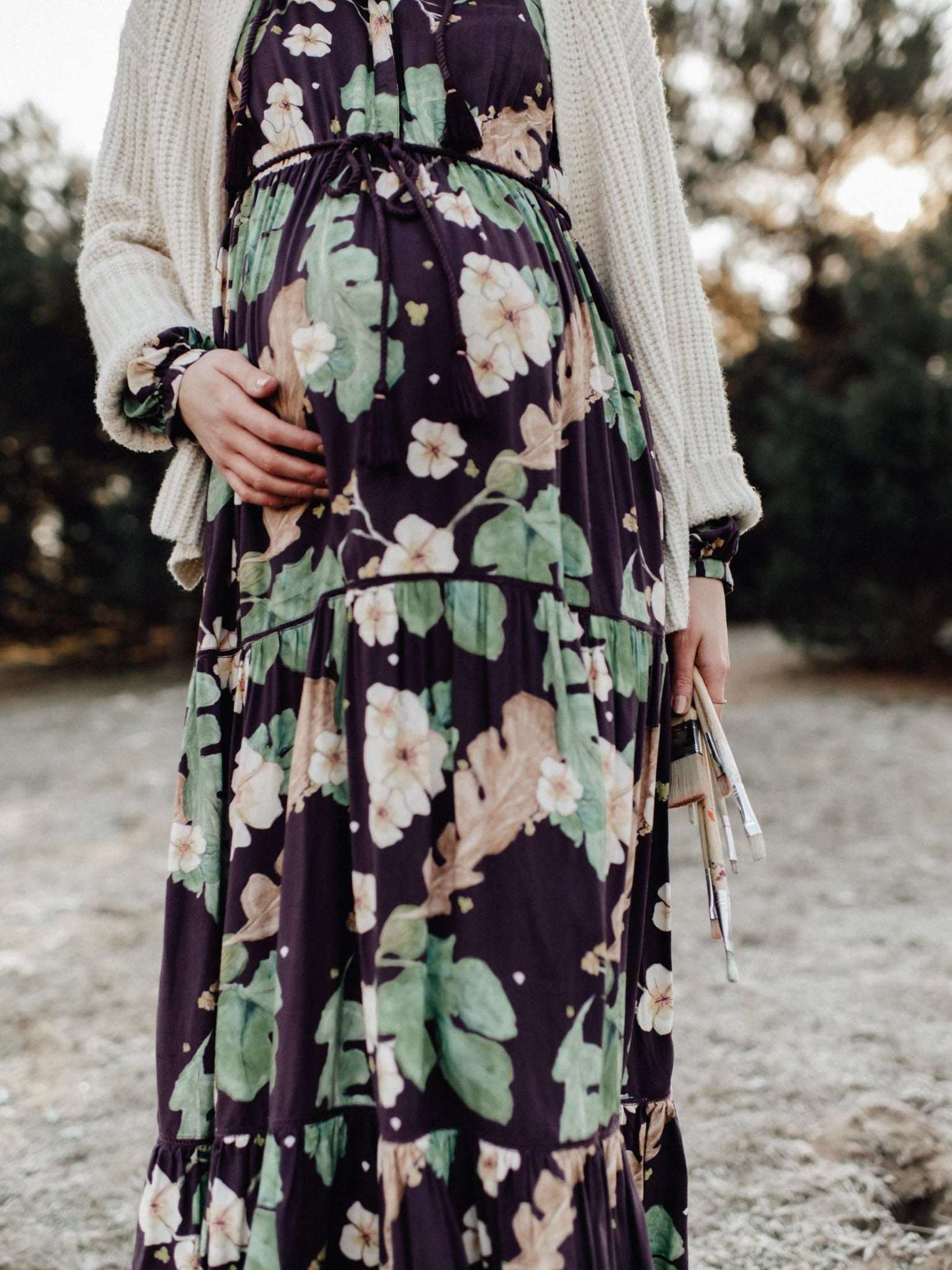 Mutterkleid Mara Mea Maxikleid für Schwangerschaft- und Stillzeit auberginefarben mit Strickjacke kombiniert, in Nahaufnahme am Strand gezeigt