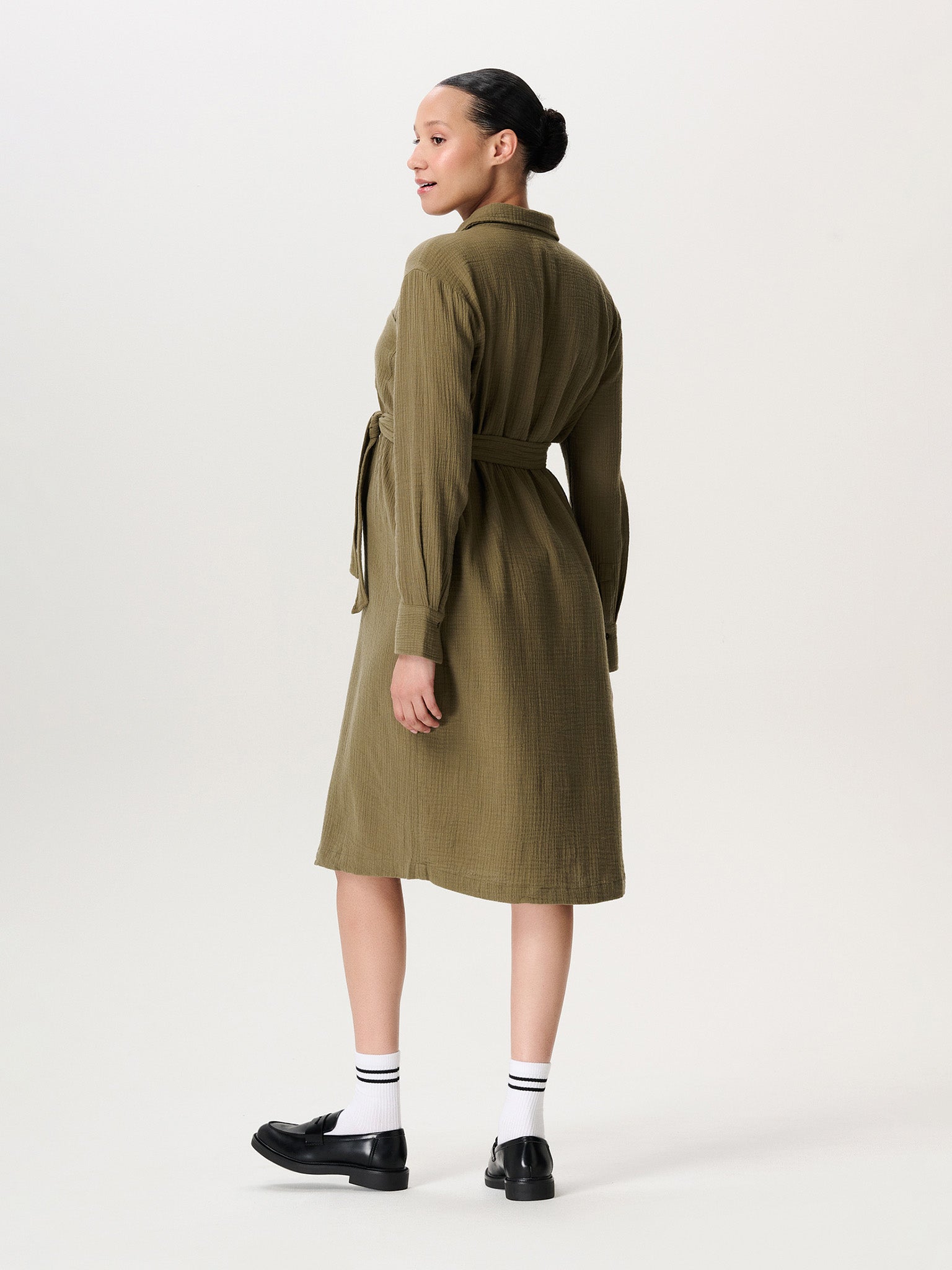 Schwangere Frau im Noppies Musselinkleid Midi-Länge, sanft fallender Stoff und betonter Babybauch. Umstandskleid kaufen oder mieten.