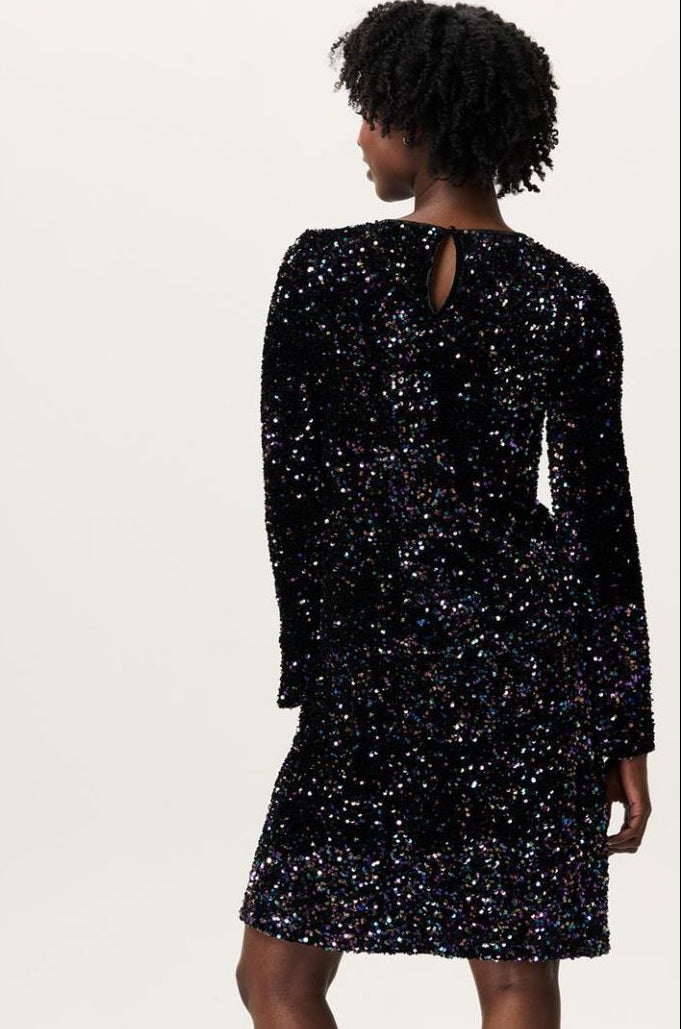 Model zeigt den Rücken des Paillettenkleids mit Knopfdetail am Nacken, schimmernde Textur im Licht