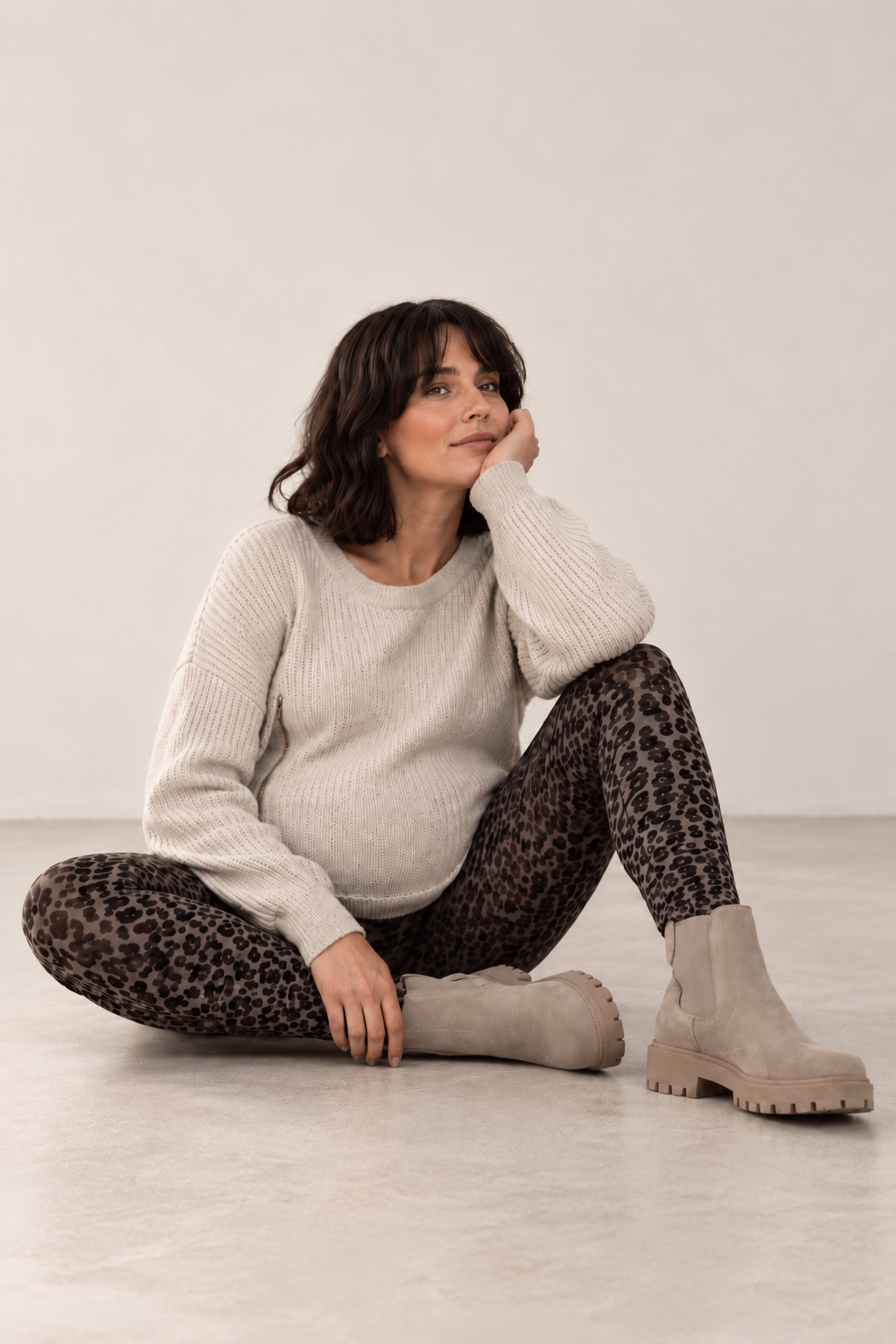 Schwangere Frau in Leo Umstandsleggings und beigem Strickpullover. Herbst Styles bei Mutterkleid