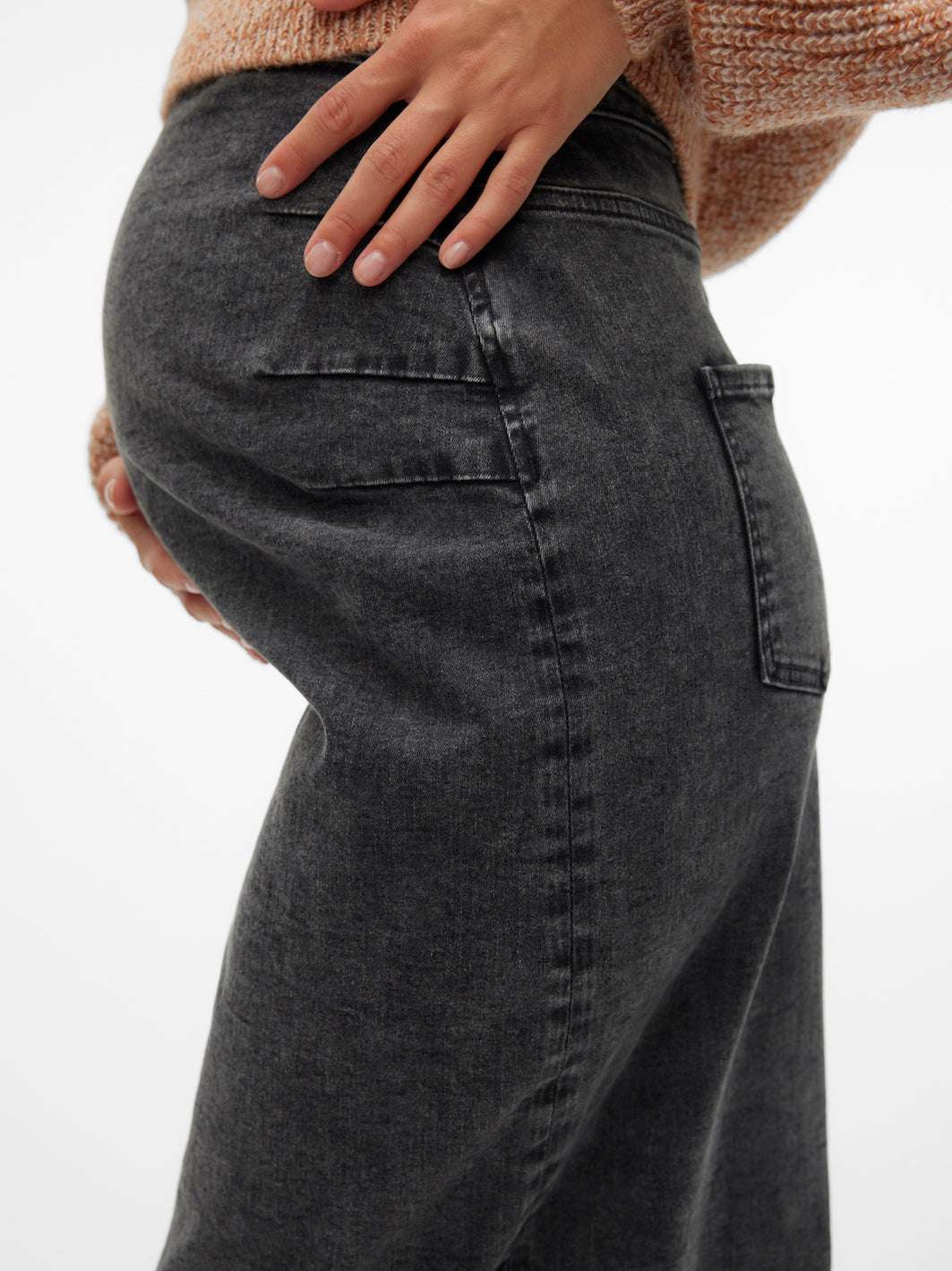 Detaillook des Mamalicious Umstands-Jeansrock in dunkelgrau. Model zeigt den Rock im Profil, Hände am Babybauch. Bei Mutterkleid online zu kaufen.