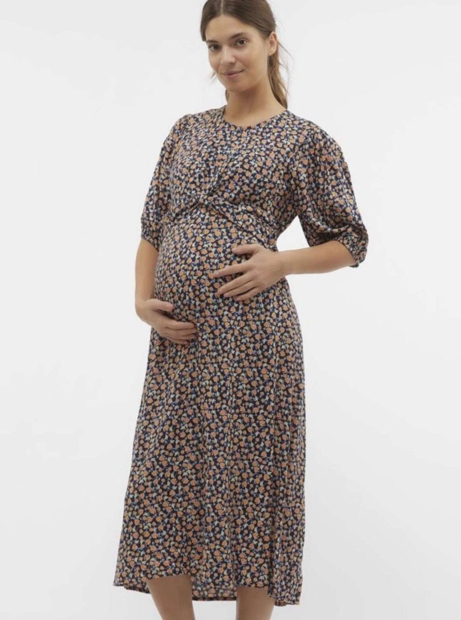Mamalicious Umstandskleid zeigt Model mit Händen am Babybauch. Kleid hat Knotendetial vorne und kurze Ärmel, jetzt mieten oder kaufen bei Mutterkleid.