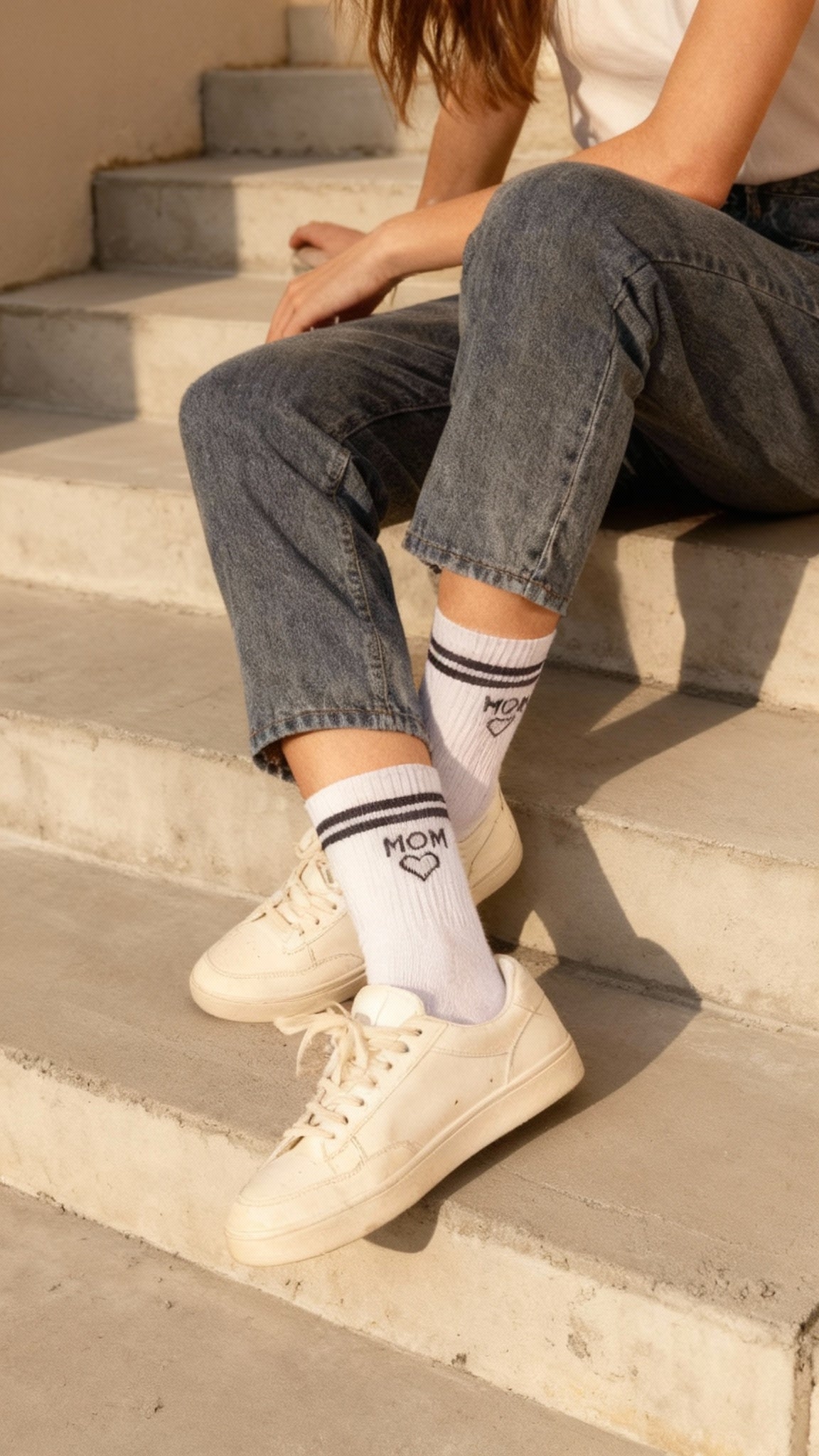Frau mit grauer Jeans und weißen Sneakern trägt Statement MOM Socken mit Herz
