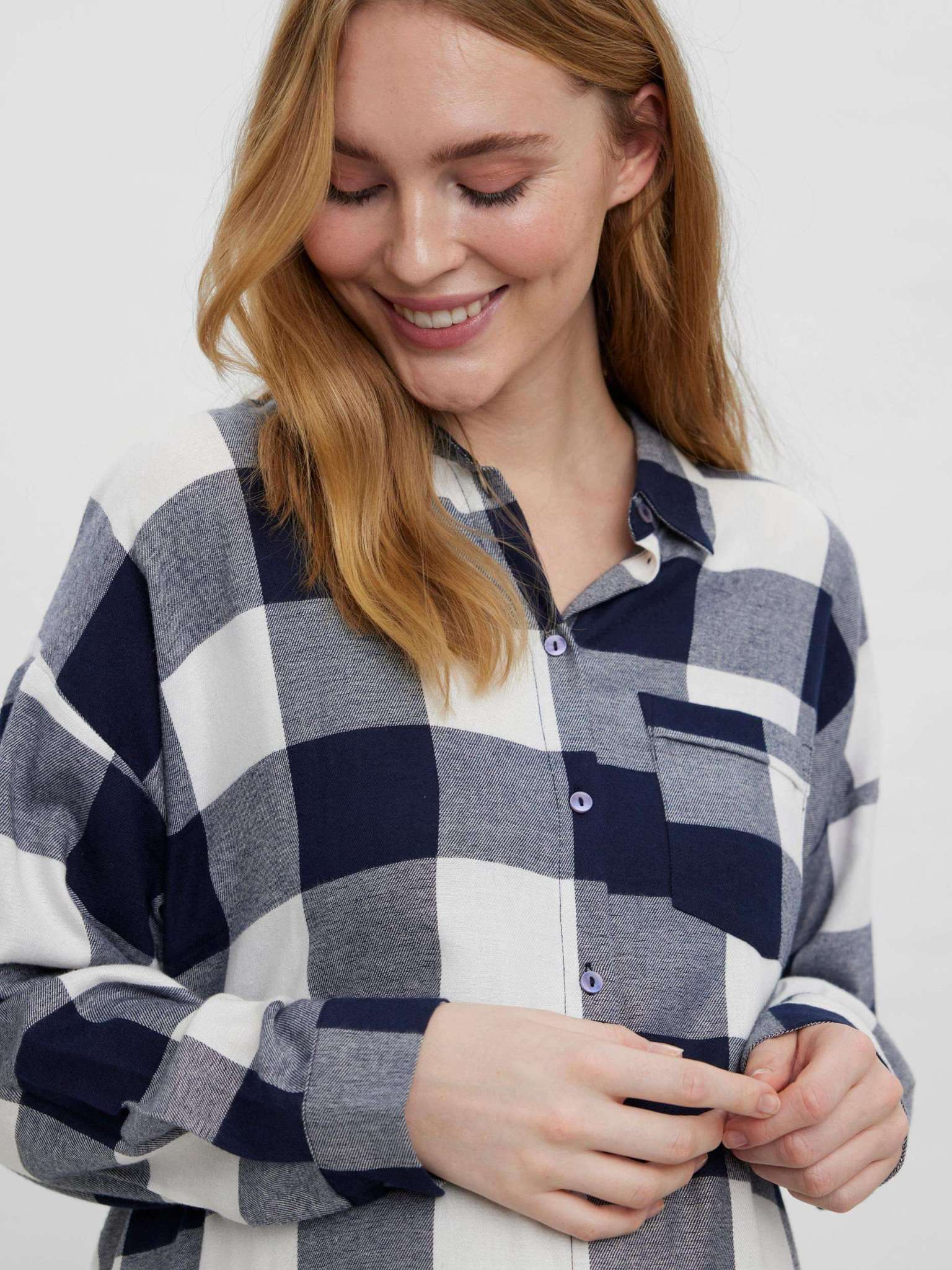 In Detailaufnahme zeigt lächelndes Model das VERO MODA MATERNITY kariertes Umstandshemd aus Bio-Baumwolle und Viskose in navy mit Knöpfen für Schwangerschaft und Stillzeit