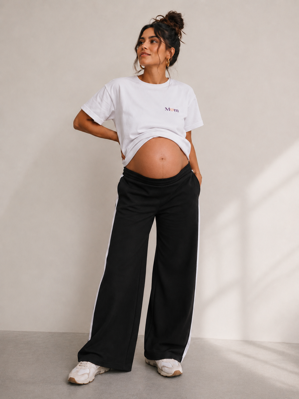 Schwangere Frau im weißen Mom Stillshirt und schwarzer Wide Leg Umstandshose mit Seitenstreifen