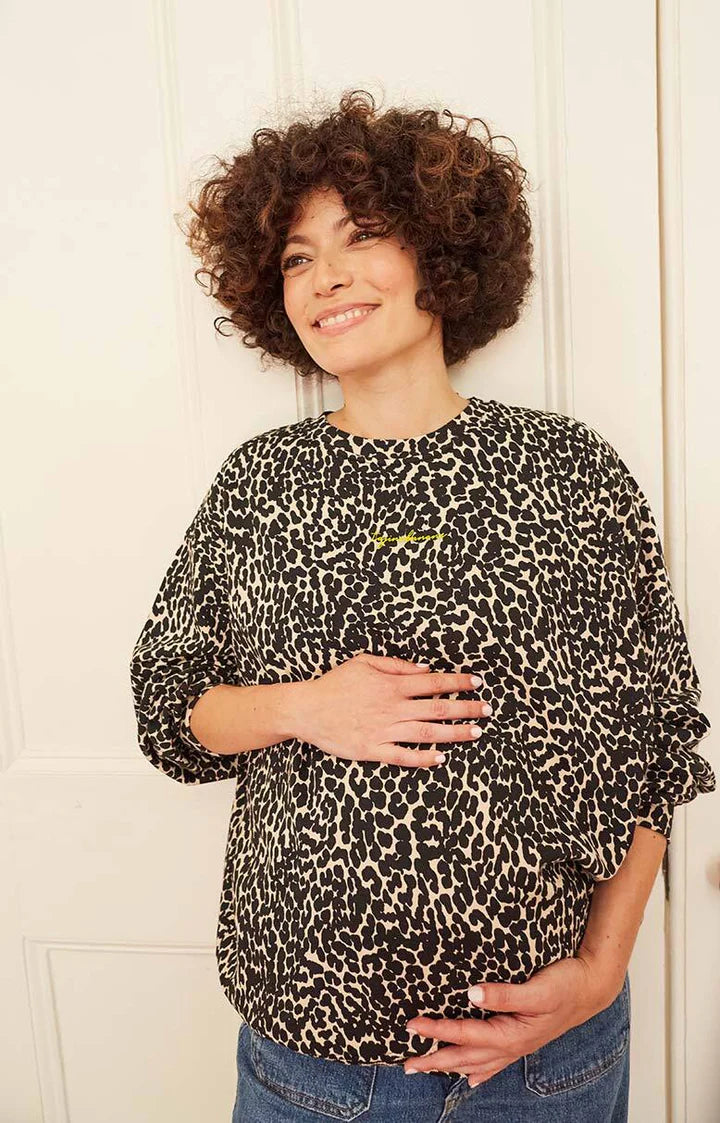 Model mit kurzen Locken lächelt und trägt Tajinebanane Umstandssweatshirt. Kaufen oder Mieten bei Mutterkleid.de
