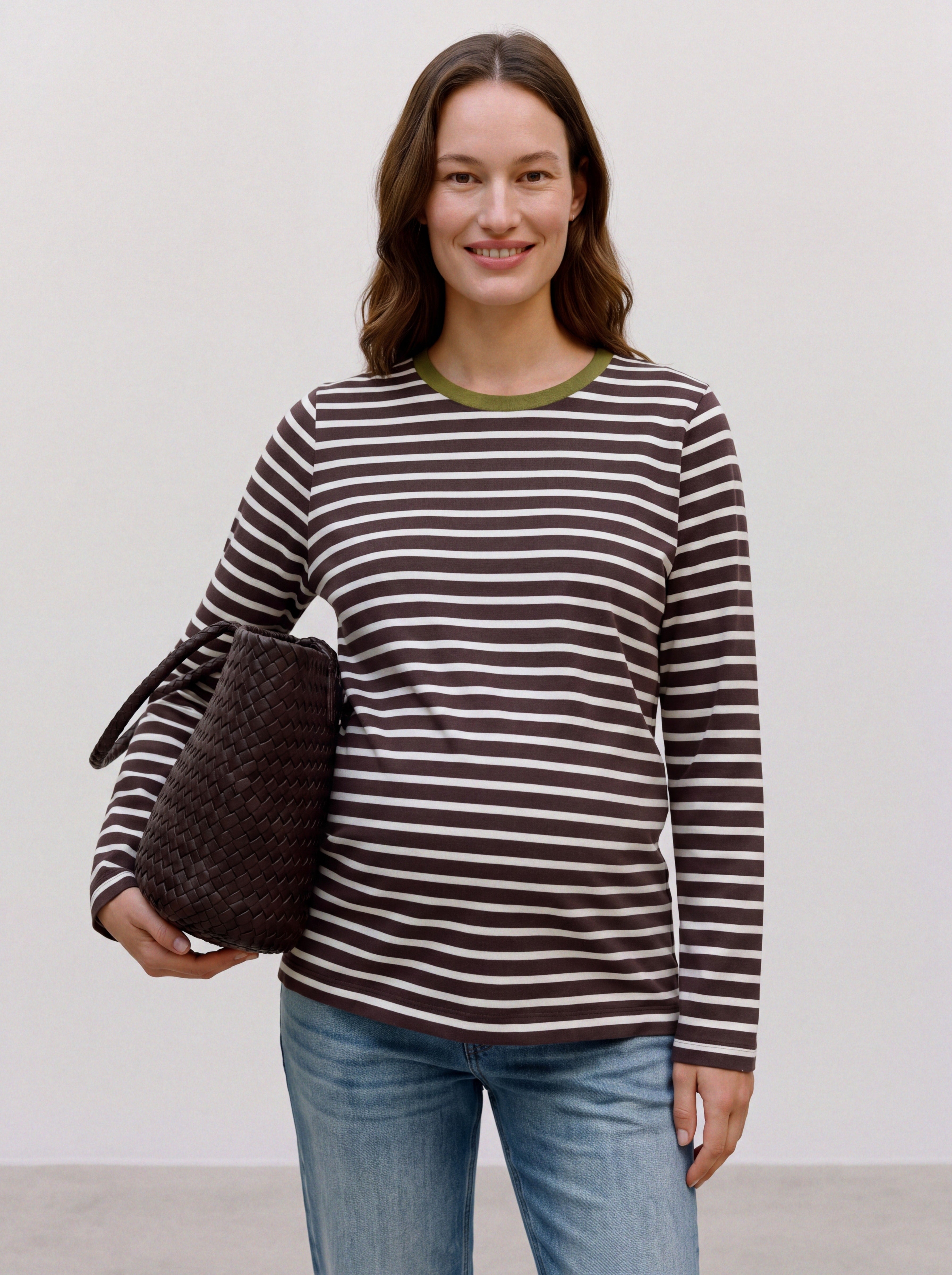 Schwangere Frau trägt gestreiftes Umstands-Longsleeve aus Baumwolle mit grünem Rundhalsausschnitt und Jeans
