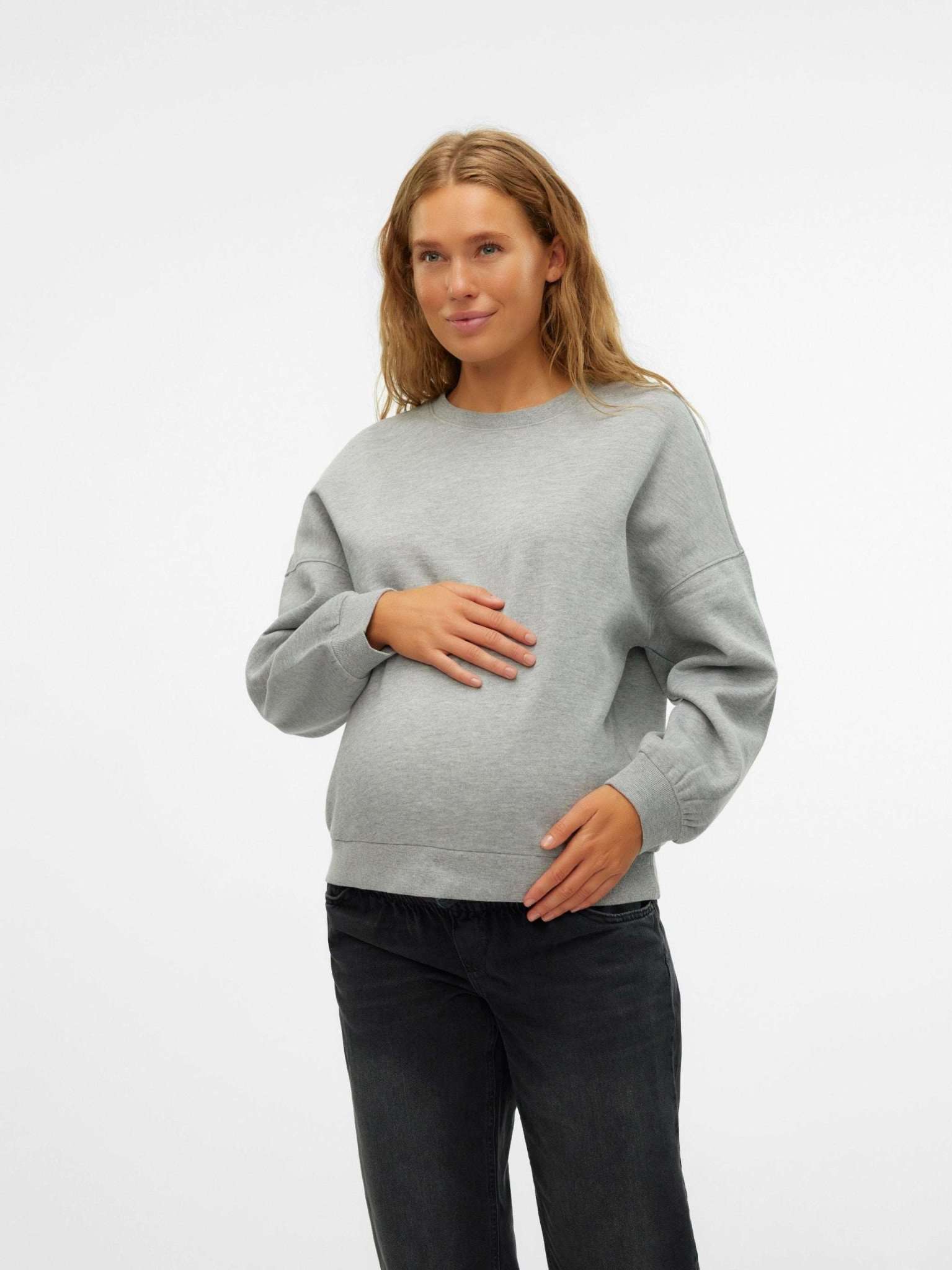 Frau mit Babybauch lächelt und trägt einen grauen Umstandspullover im Sweater Style