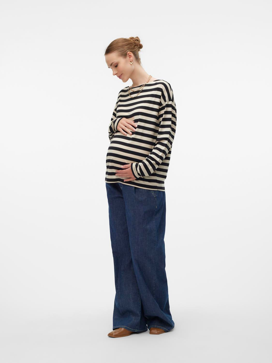 Schwangere Frau mit Babybauch stylt gestreiftes Langarm Umstandsshirt aus Lyocell zu blauer Wide Leg Umstandsjeans